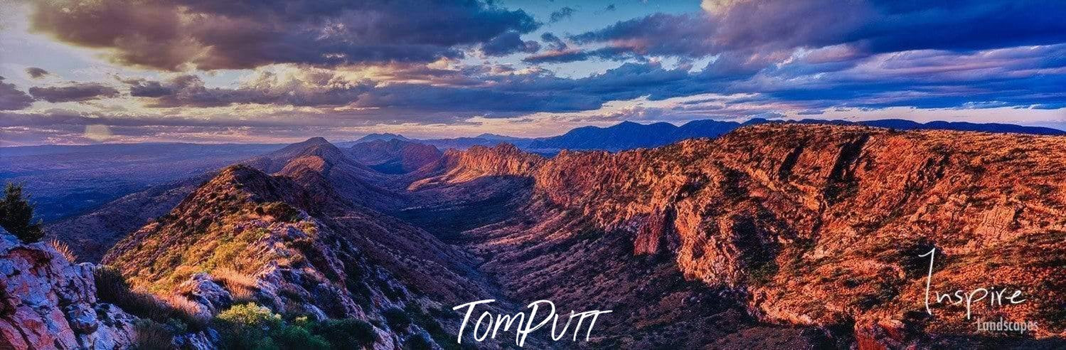 A long series of cliffs with a cut mountain in between and dense clouds over them with some sunshine hitting on the right side, Counts Point, Larapinta Trail - West Macdonnell Ranges, NT