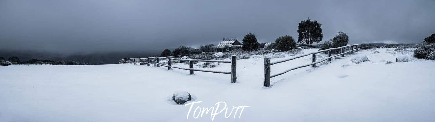 A beautiful snow-covered area with the fence of wood around it, some trees and a small house inside, Craig's Hut Panorama - Victorian High Country