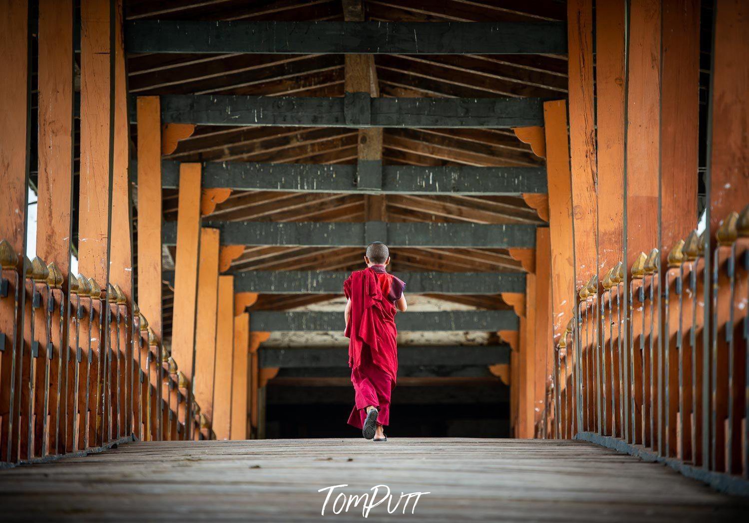 A man with red attire crossing a wood bridge of brown color with green color ceiling, Crossing, Bhutan 