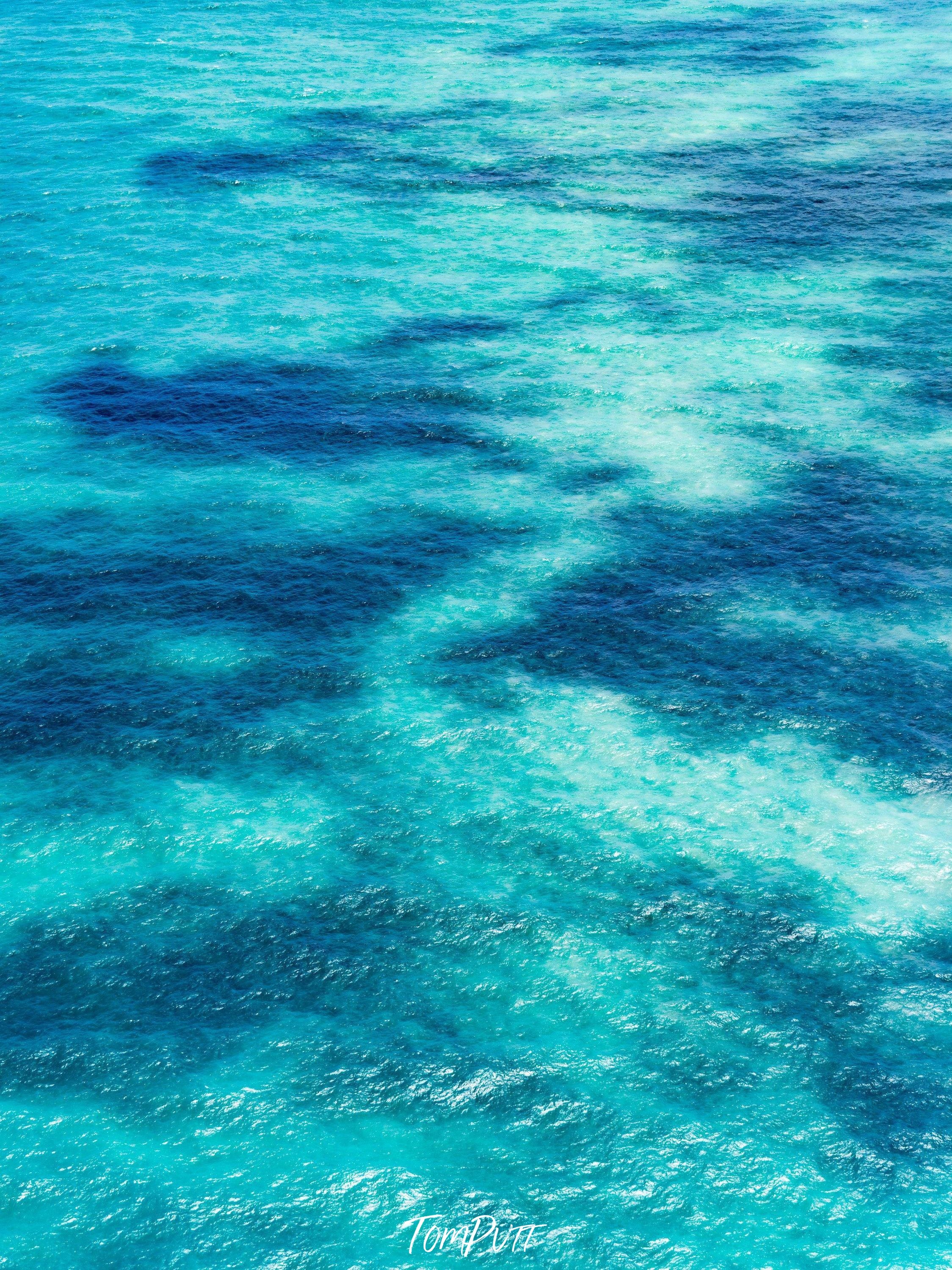 A shiny sky-blue ocean with the parallel shadow of some random shapes inside the water, Dancing Shadows 