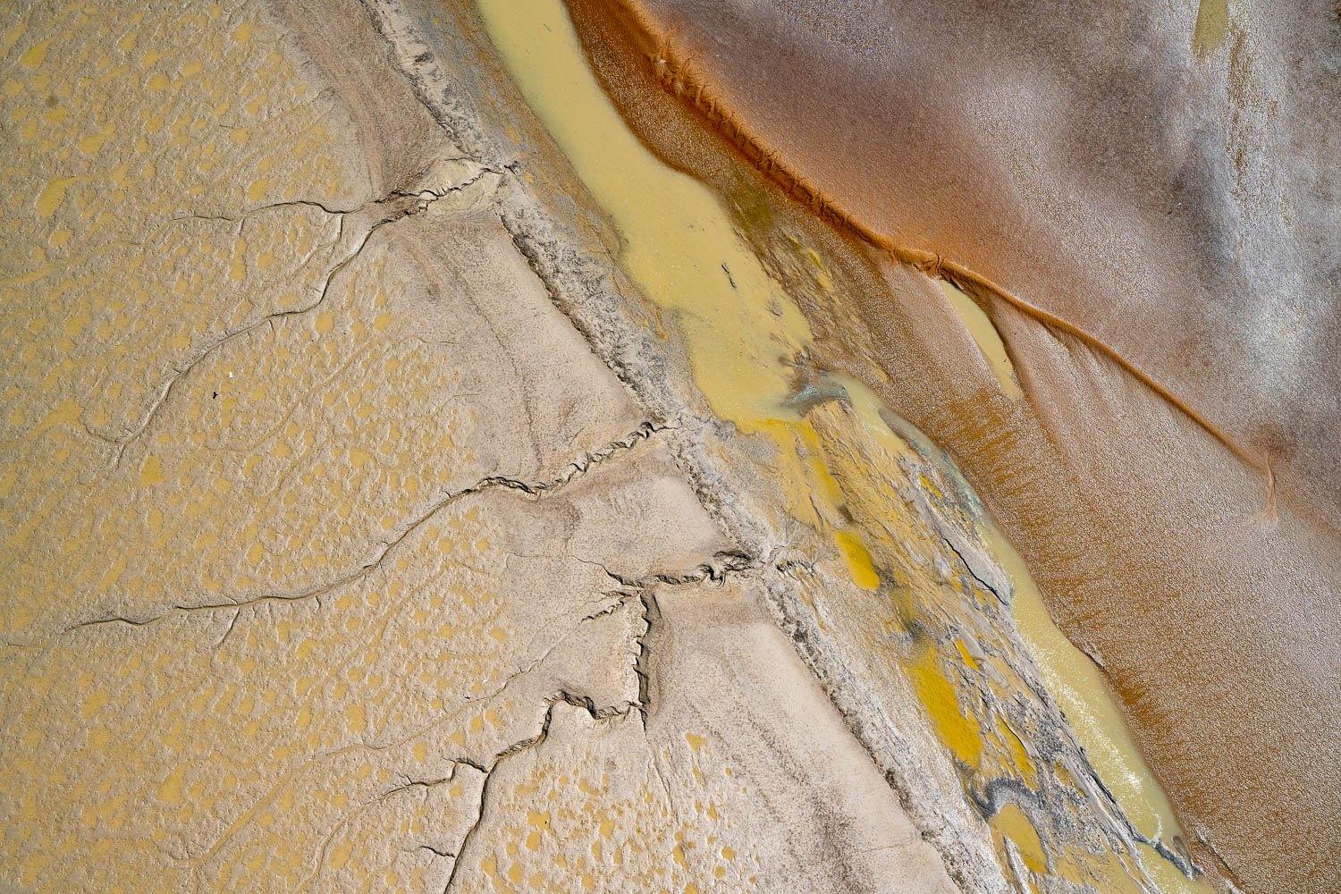 An aerial view of a desert-like land with some long cracks and a yellow and orange line of sand on it, Derby #13
