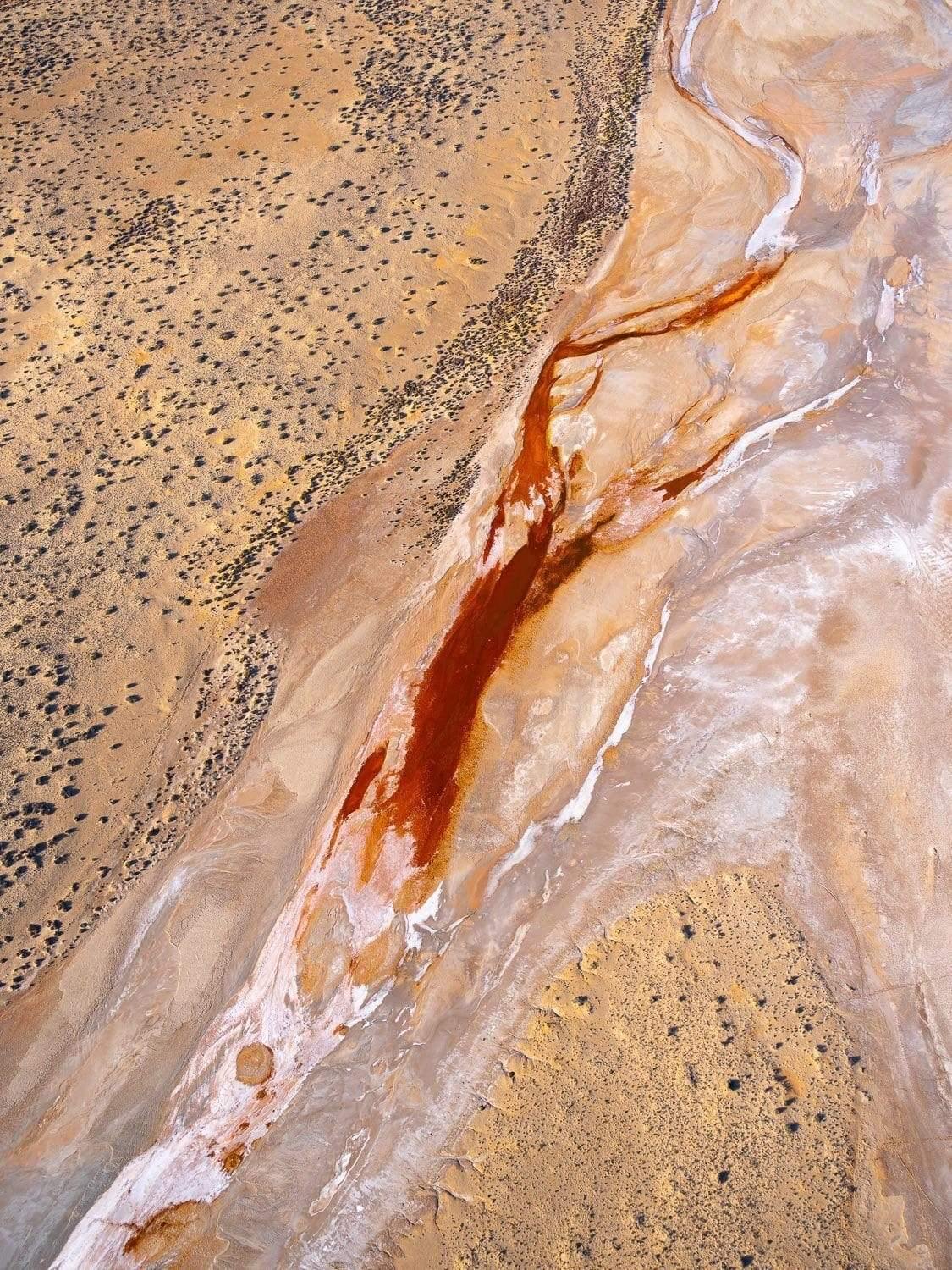 A portrait of large desert land with countless small stones and their shadows, a bloodline-like centric area with some dark brown liquid and smoky outlines around it, Desert Flame