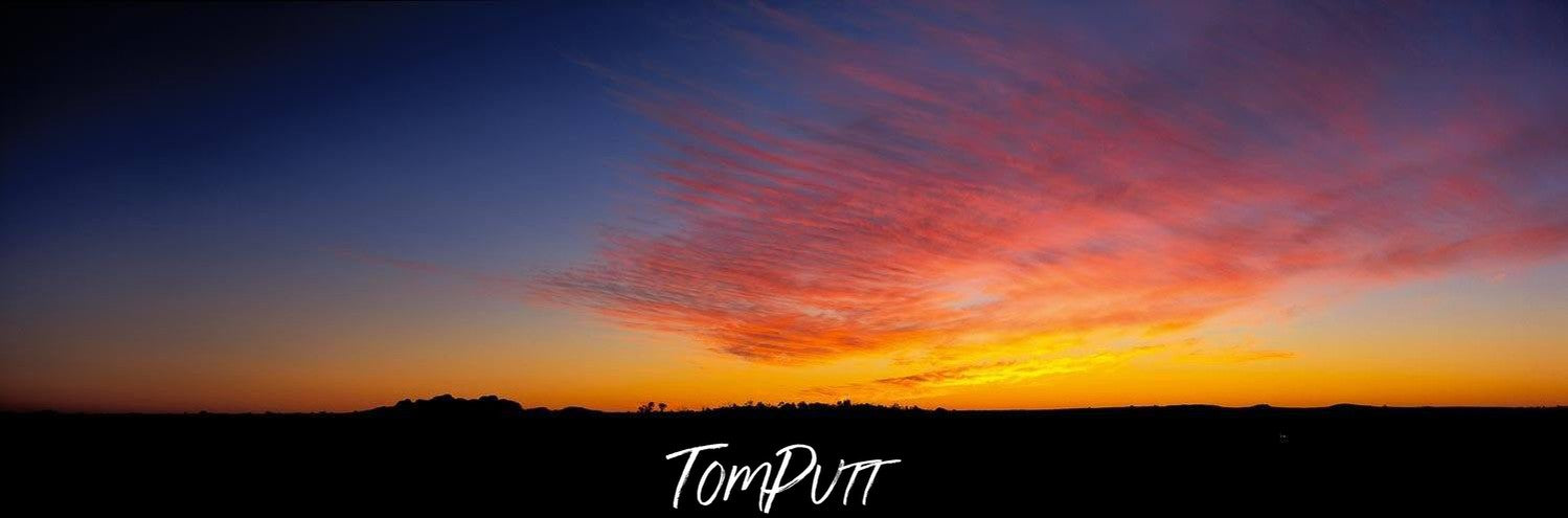 A wide desert area with under dark black shadows, an effect of sunset with orange and yellowish effect in the far background, Desert Sunset - Red Centre NT