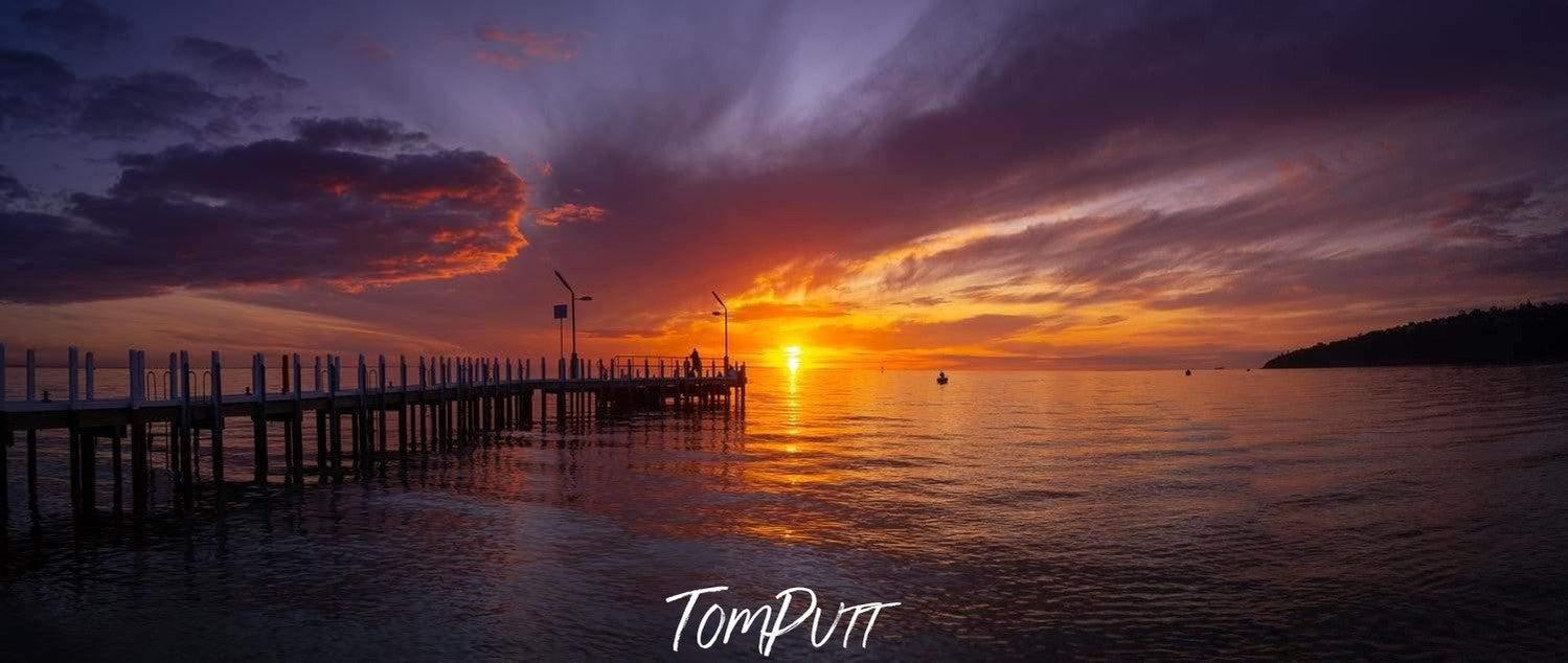 A long wood bridge over the sea, and a beautiful yellowish and orangish effect of the sunset in the far background, Dragon's Breath, Safety Beach - Mornington Peninsula VIC