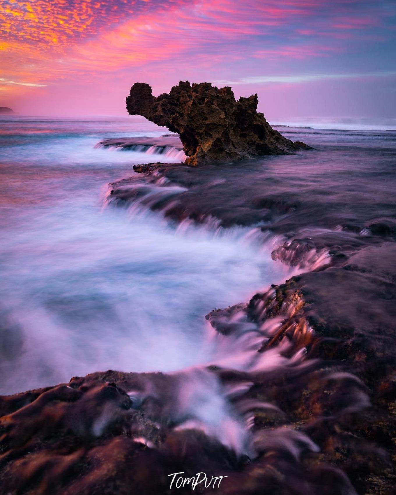 A long mountain wall with steady waterfalls passing over the wall, and a dragon's head like design is forming by the mountain in the background, and some pinkish effect forming on the sky, Dragon's Flame, Rye - Mornington Peninsula VIC