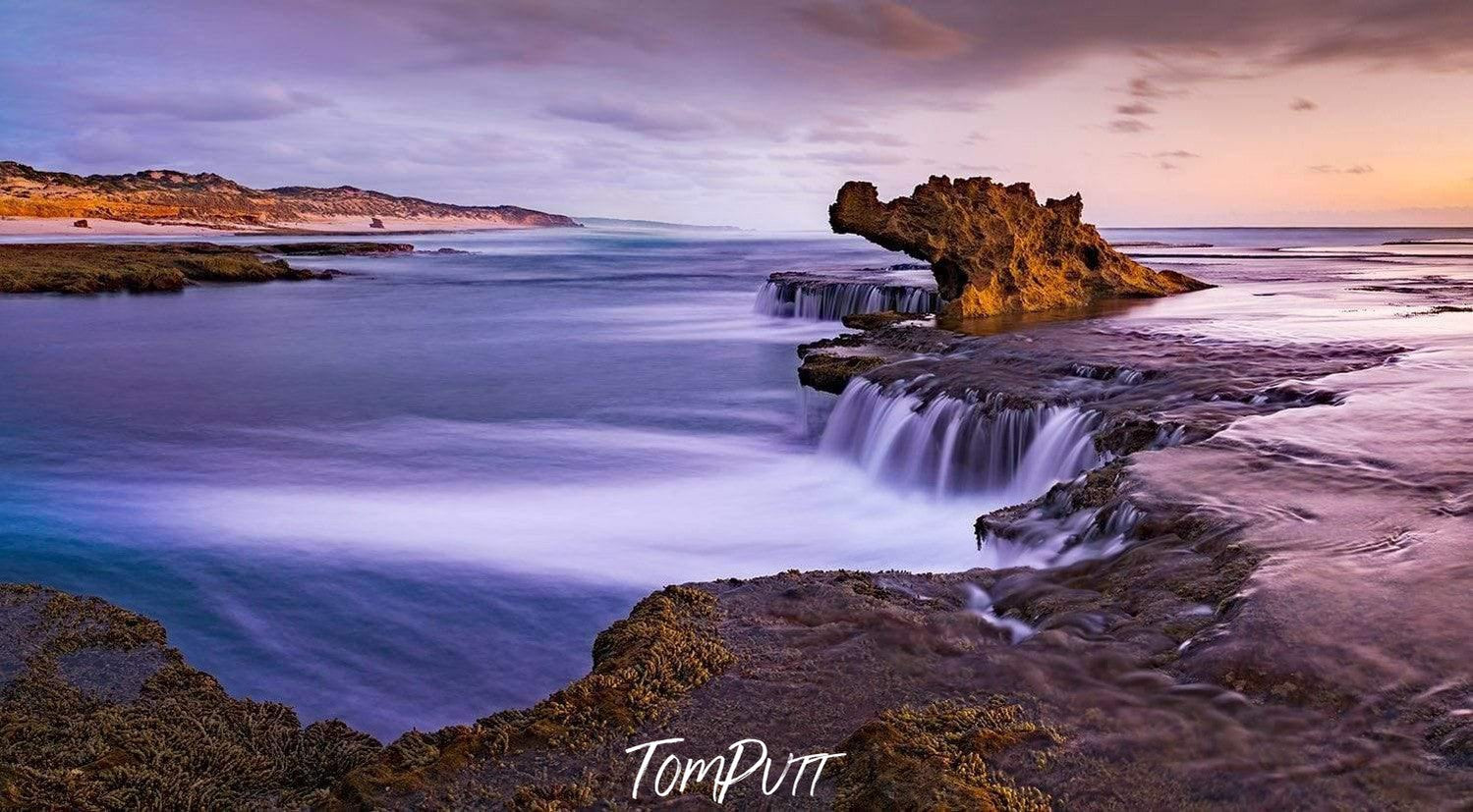 A long mountain wall with steady waterfalls passing over the wall, and a dragon's head like design is forming by the mountain in the background, and some sand-color effect forming on the sky, Dragon's Flame, Rye - Mornington Peninsula VIC