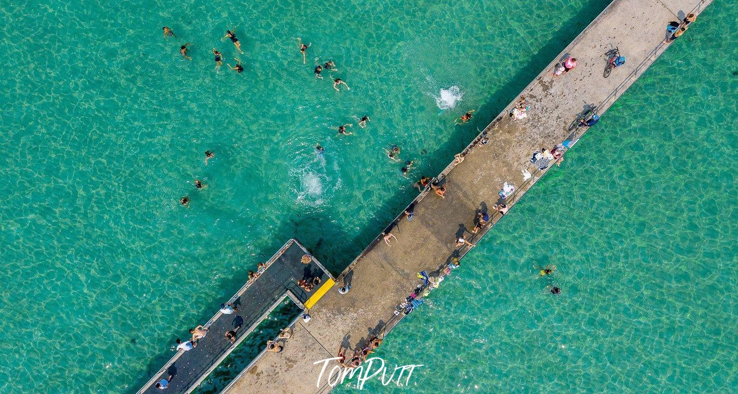 An aerial view of a bridge over the green-colored ocean, a number of people on the bridge and some on the water, Dromana Pier - Mornington Peninsula VIC