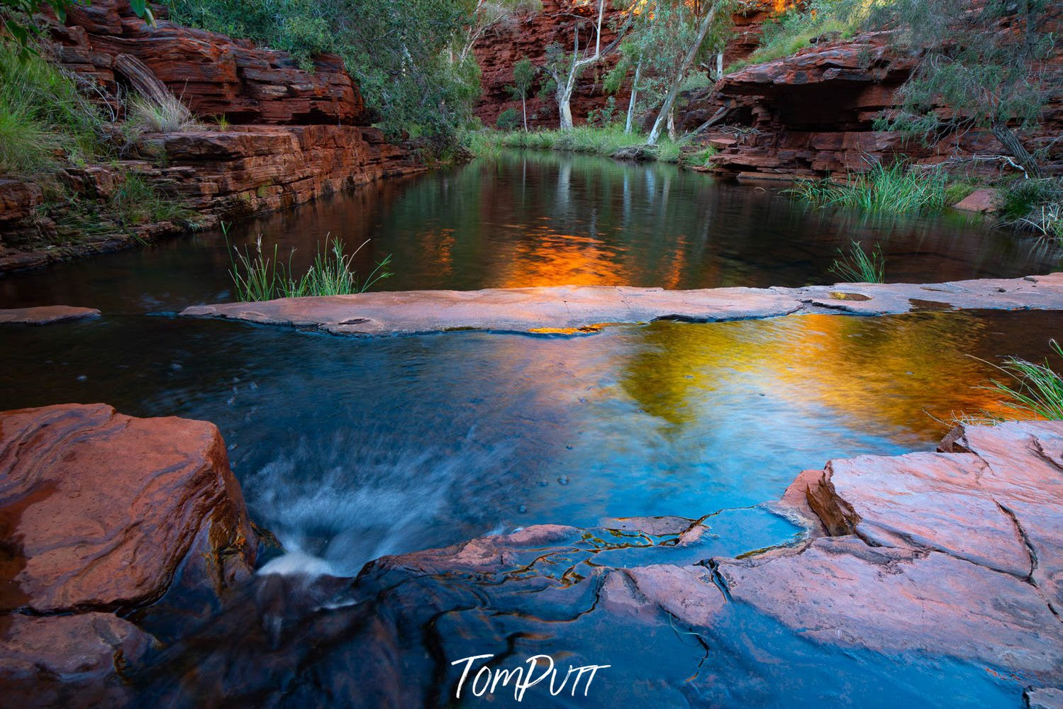 A beautiful watercourse with some flat stones in the water, and a long red-bricked mountain wall with some greenery behind the watercourse, Early morning glow, Weano Gorge - Karijini, The Pilbara