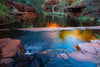 A beautiful watercourse with some flat stones in the water, and a long red-bricked mountain wall with some greenery behind the watercourse, Early morning glow, Weano Gorge - Karijini, The Pilbara