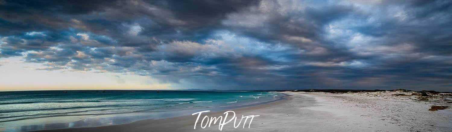 A landscape view of a beach with sky-blue water, Giant ice-blue and grey dense clouds over the scene, Eddystone Beach panorama, Bay of Fires