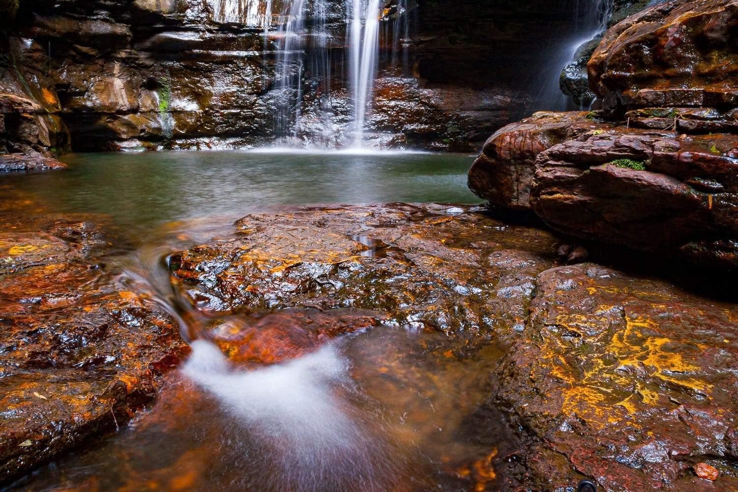 A beautiful waterfall from rock of orange and dark brown shade, some flat stones on the ground with the overflow of the water, Empress Falls - Blue Mountains NSW