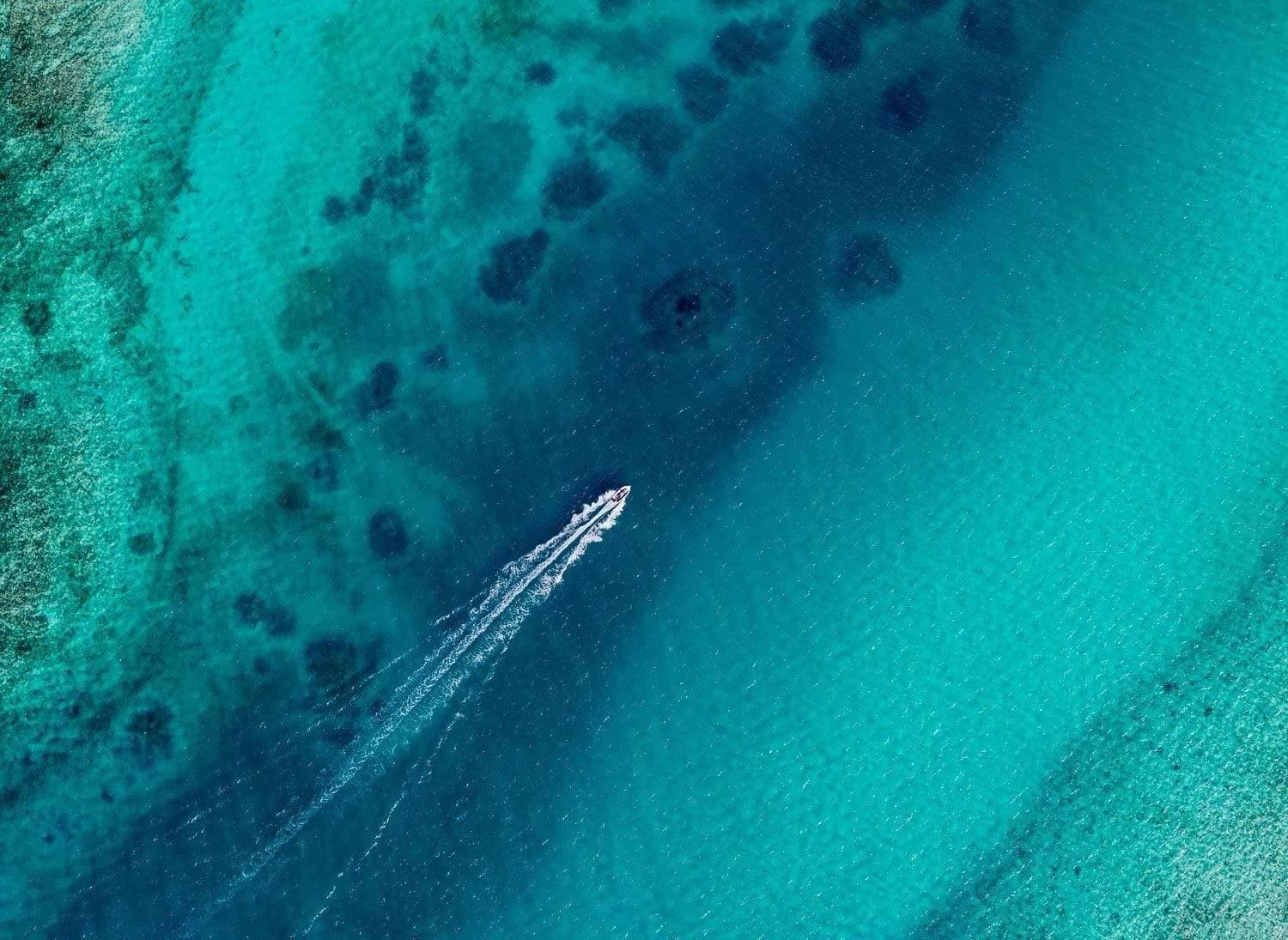 An aerial view of an ocean with only a boat floating over the surface of the water making a long mark on the surface, Escaping Houtman Abrolhos Artwork