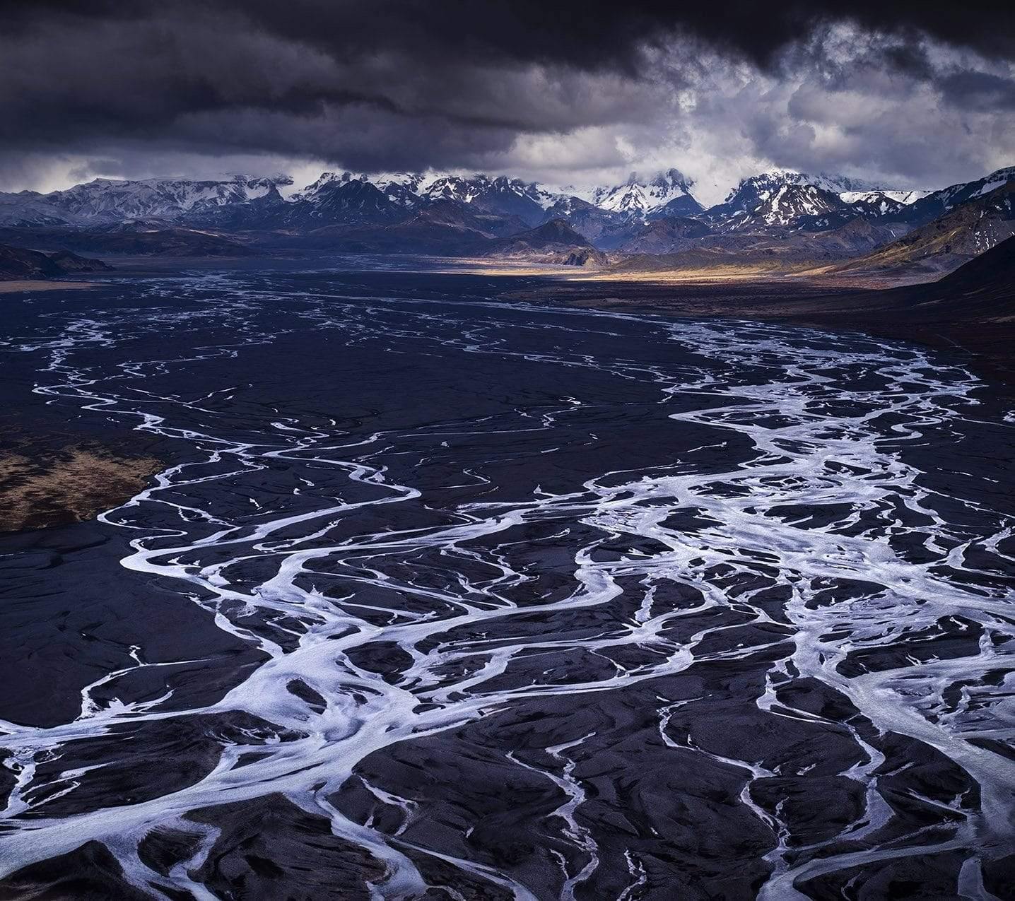 Black and white zig-zag lines and corves on the land with some high mountains with the peak covered with snow, dark stormy clouds over the picture, Glacial Melt