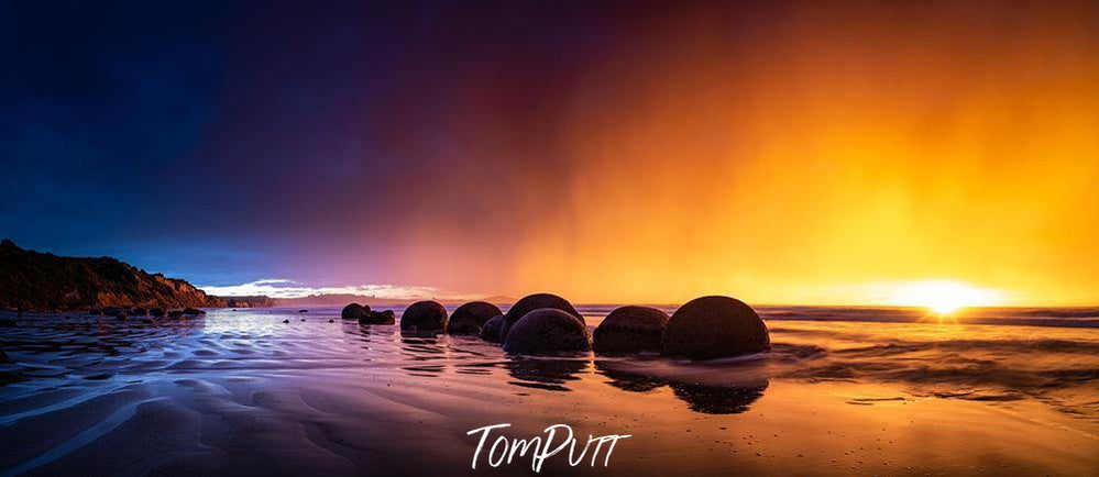 A yellow and purplish effect of sunset on a beach with a row of rounded stones, Golden Dawn, Moeraki Boulders