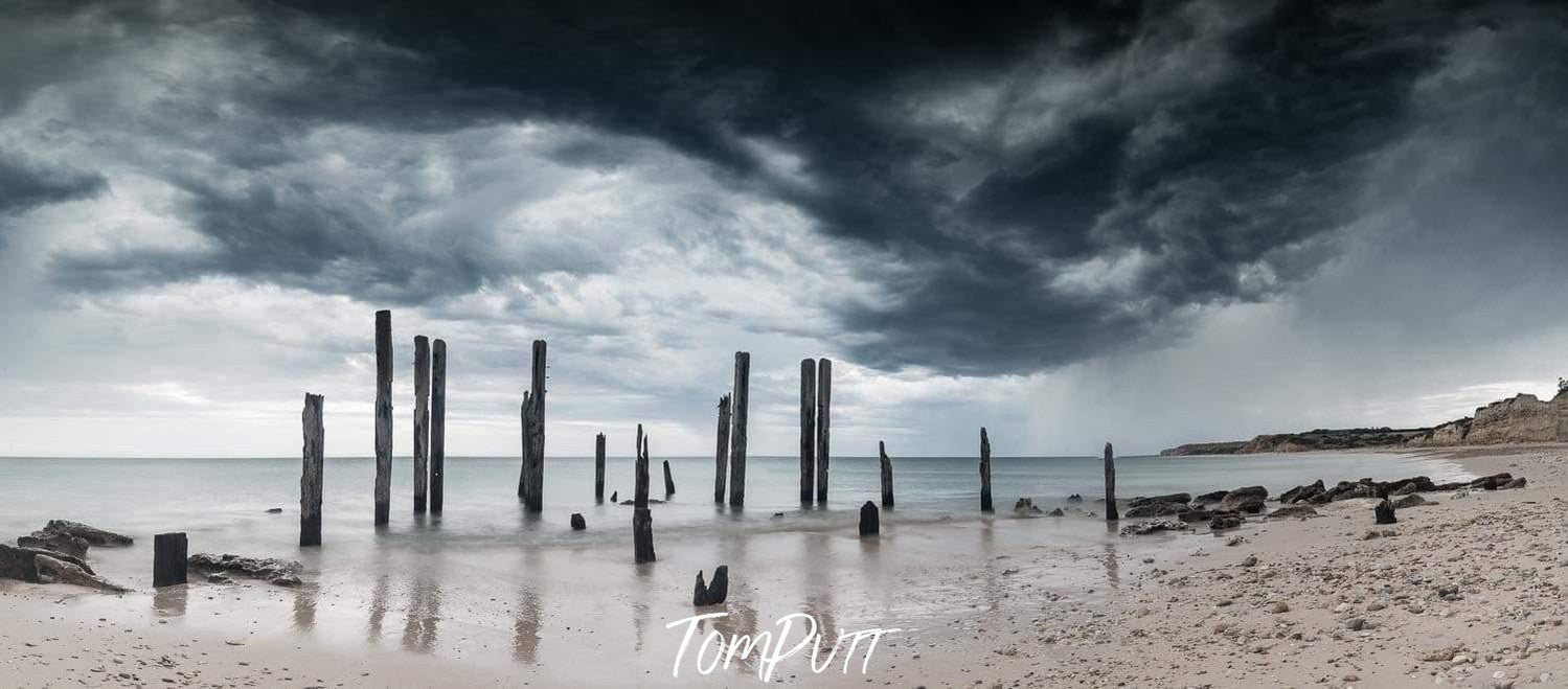 A sequence of woody pillars in the water, and dark stormy clouds over the scene, Jetty Ruins, Willunga SA