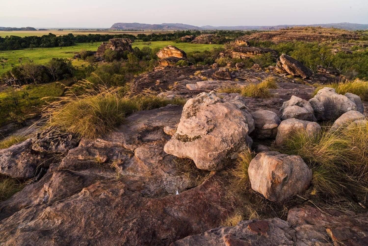 A rocky land with some stones, and a long greenfield area in the background, Kakadu Territory - Northern Territory