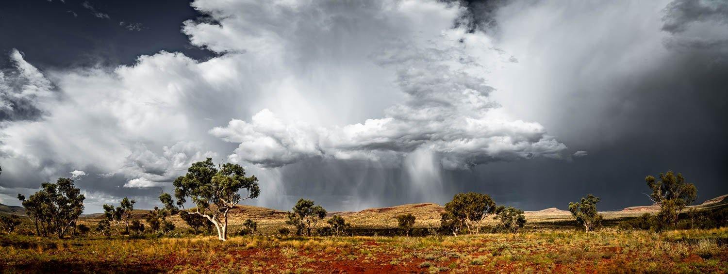 A large stony land area with some trees and a large group of smoky clouds over it, Karijini Rain - Karijini, The Pilbara