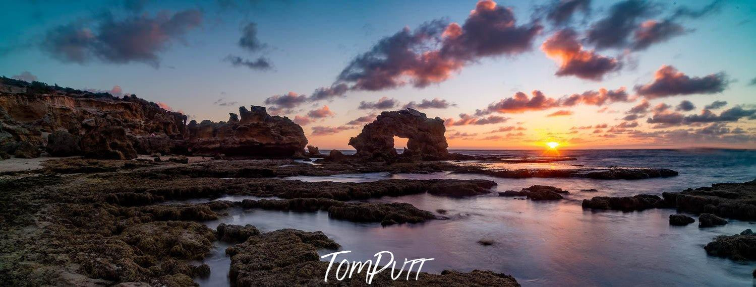 A wide sea shore with mountain stones, a large standing hollow mountain rock in the background, Keyhole Rock Sunset, Blairgowrie - Mornington Peninsula VIC 