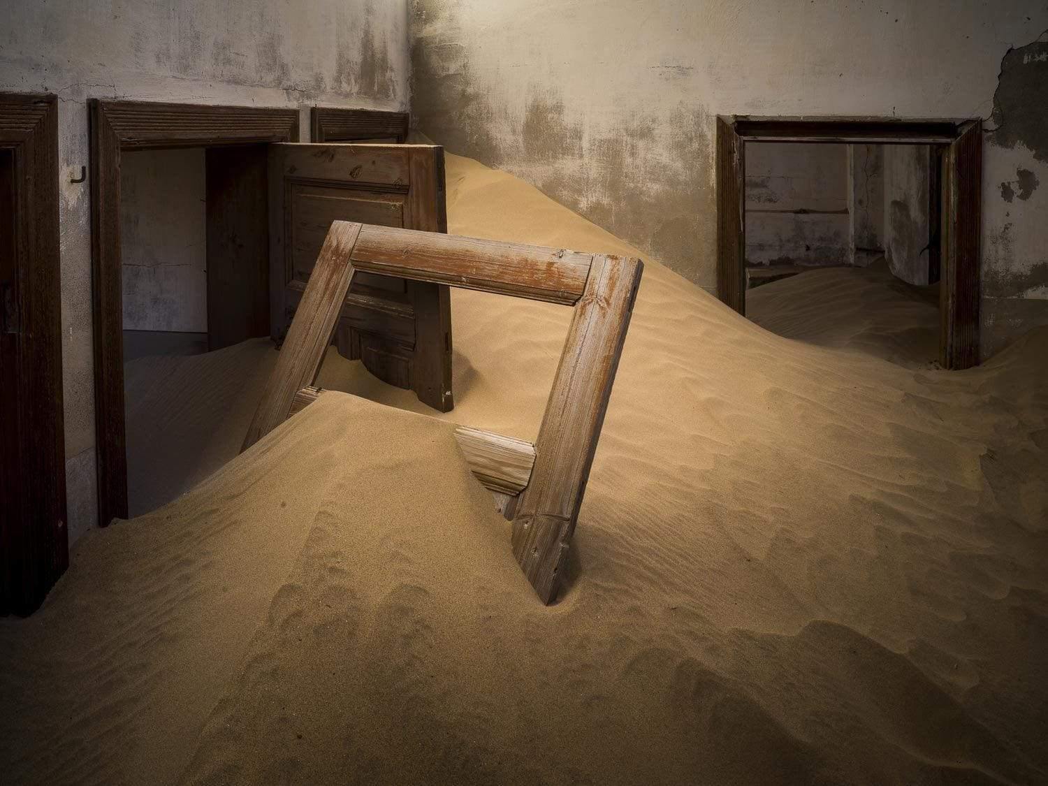 Making of a house with a lot of construction sand inside, and a broken door inside the sand, Kolmanskop #3 - Framed