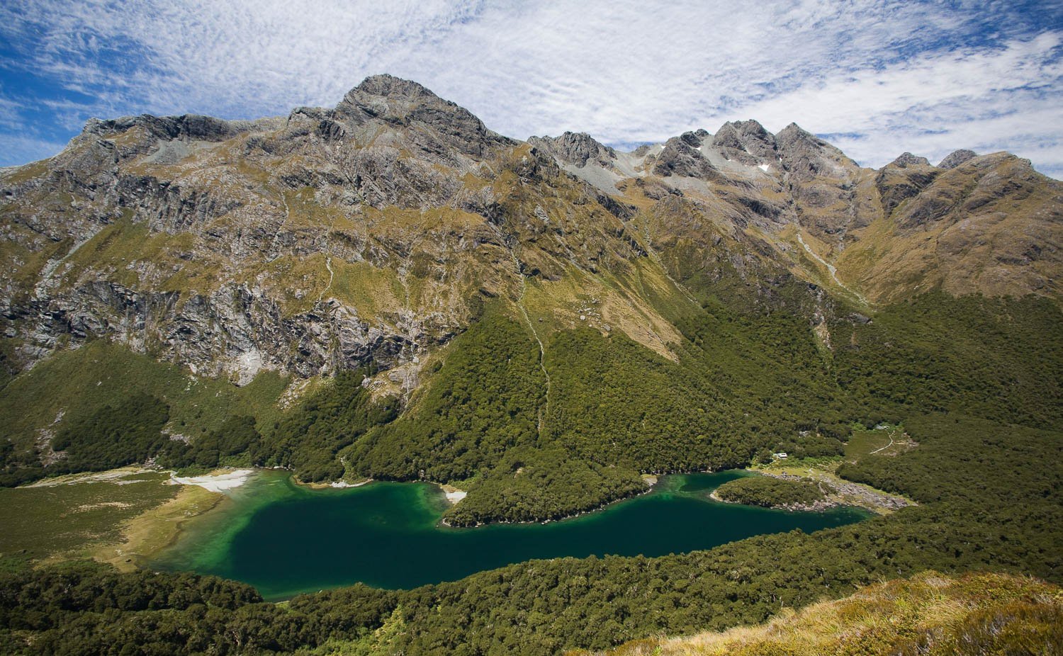 Giant green mountains with a small lake below, Lake MacKenzie from high above the Routeburn Track - New Zealand