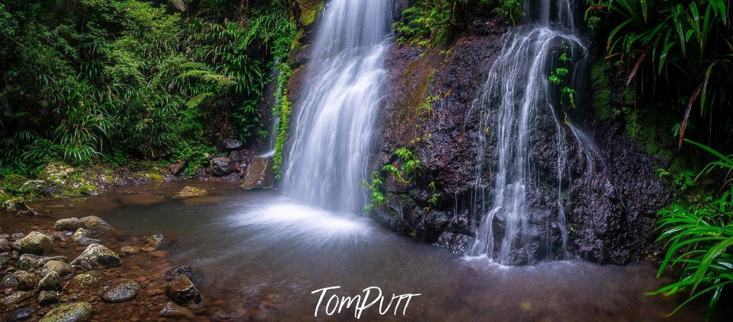 Multiple waterfalls from a green mound in a small lake, with some stones at corner, Lamington Waters - QLD