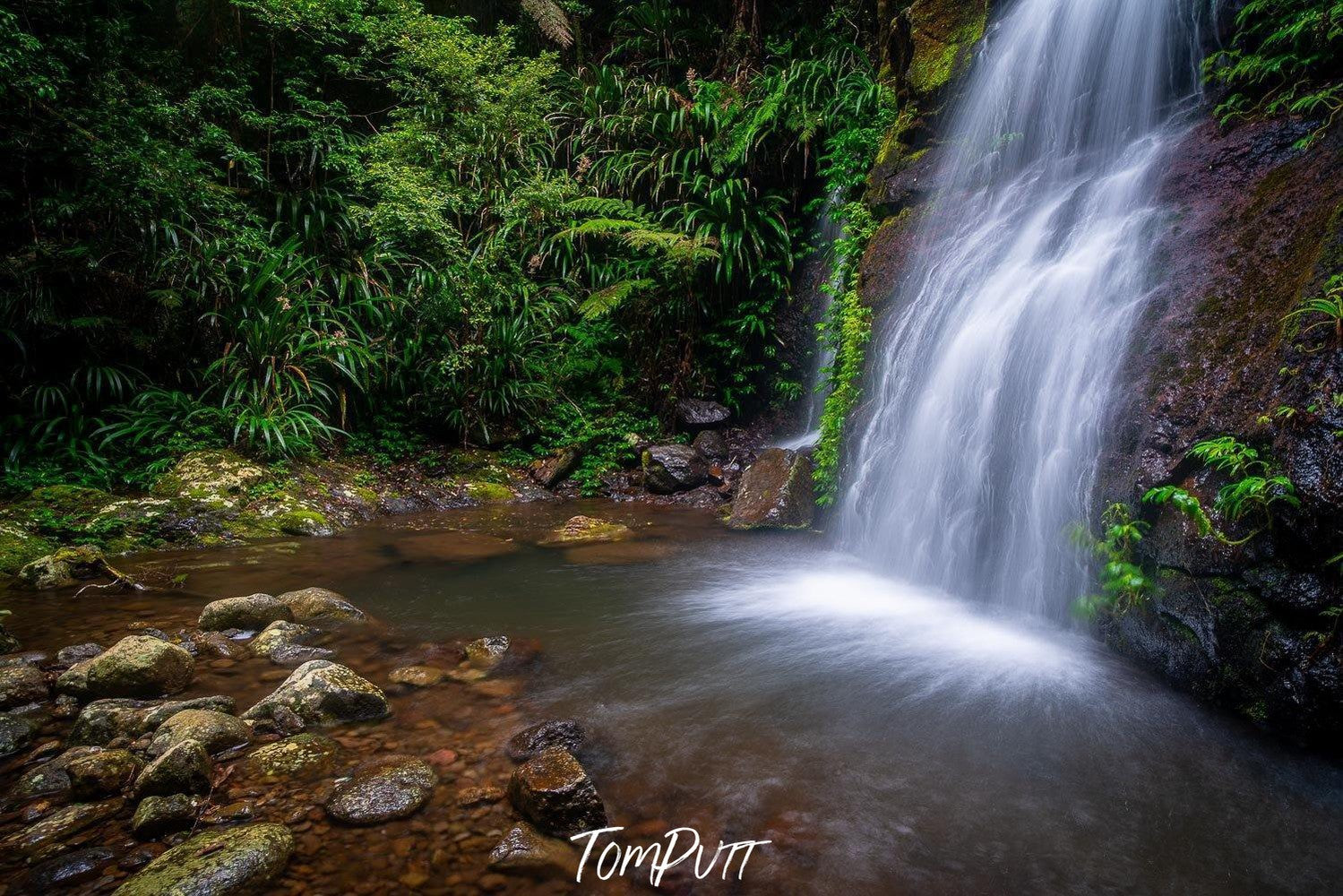 Waterfall from a green mound in a small lake, with some stones at the corner, Lamington Waters - QLD