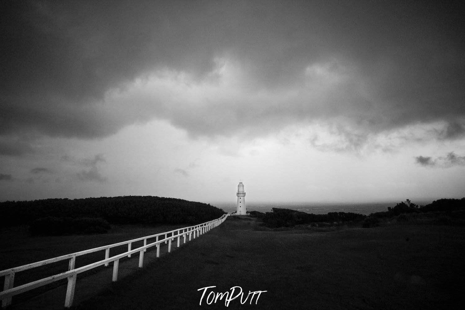 A long shot view of a lighthouse on a hill point with a group of stormy clouds over it. Lighthouse Storm, Cape Otway - Great Ocean Road VIC