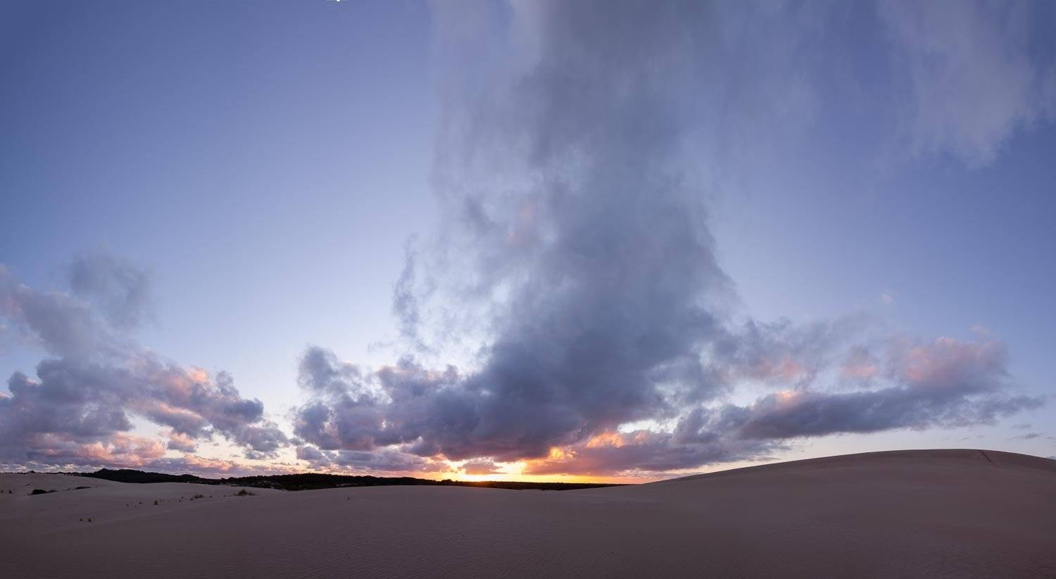 A desert with giant smoky clouds over, and a view of sunset in the far background, Little Sahara Dusk - Kangaroo Island SA