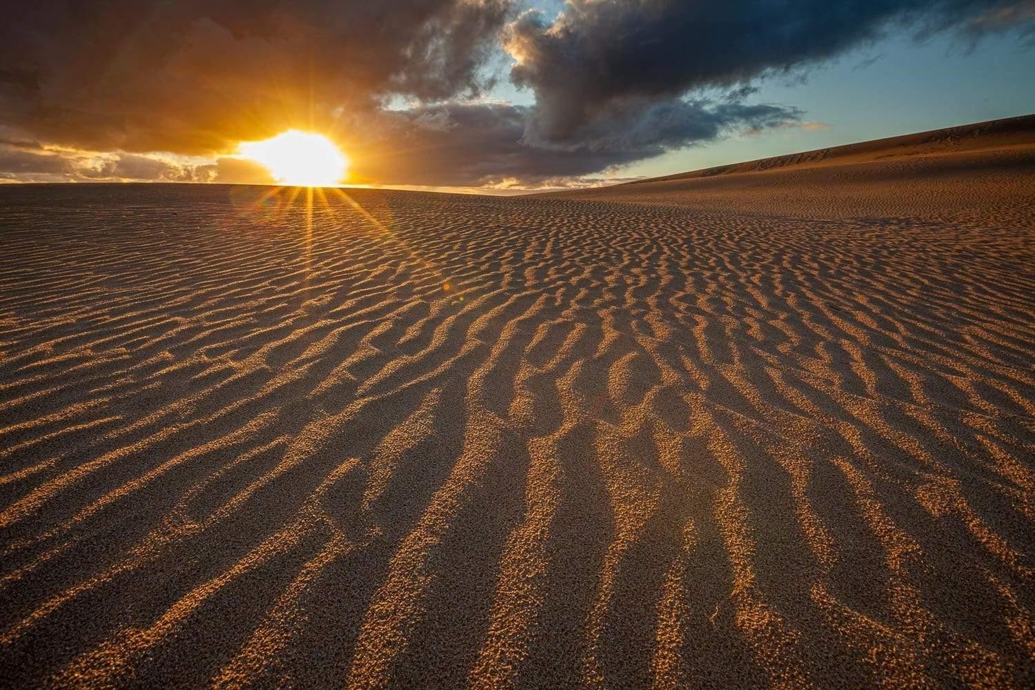 A desert with giant black clouds over with lite sunlight rays, Little Sahara Sunset - Kangaroo Island SA
