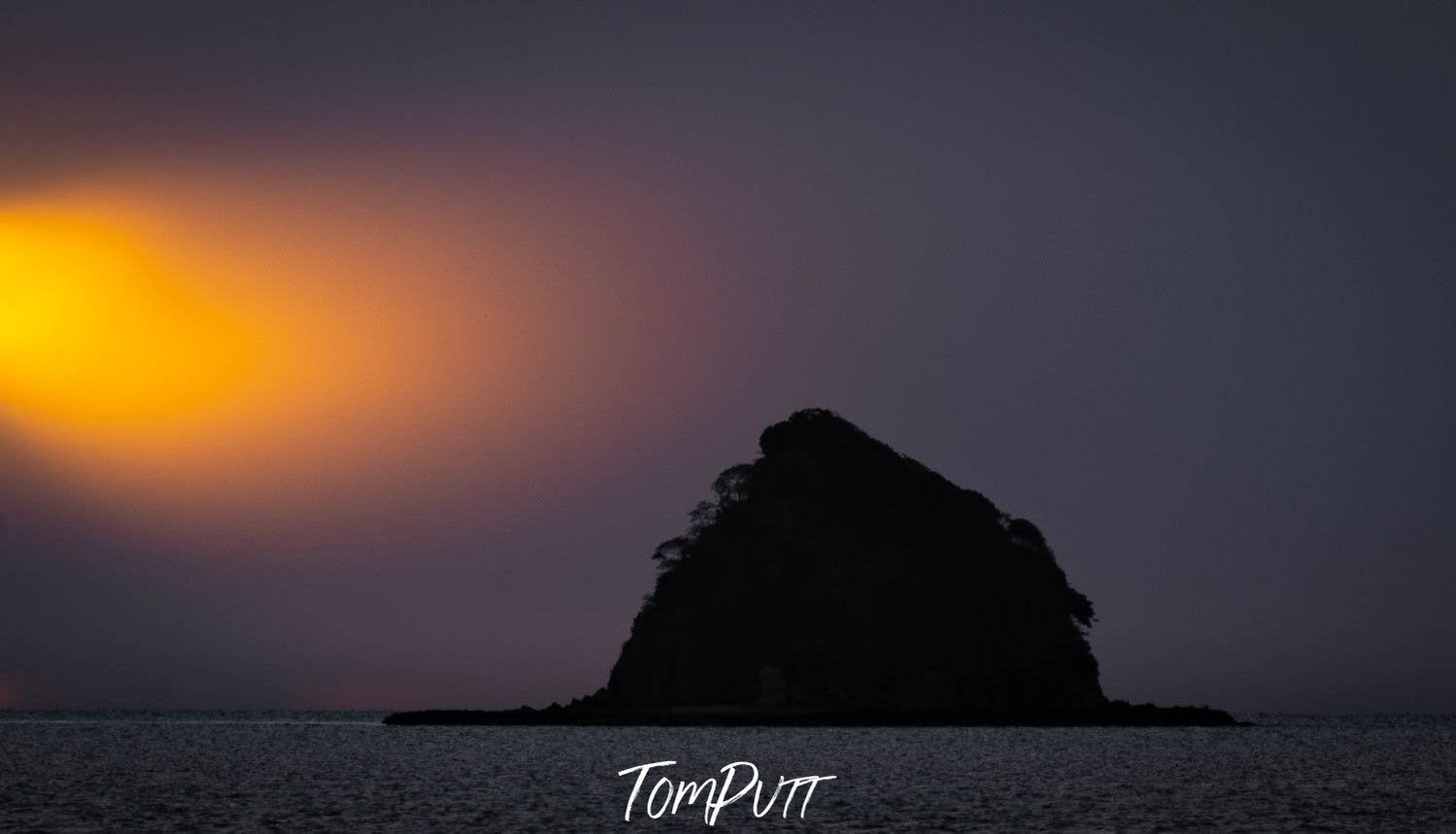 Dark view of a black mountain island with a golden shade of sunset, Lone Island off Palm Cove, Far North Queensland