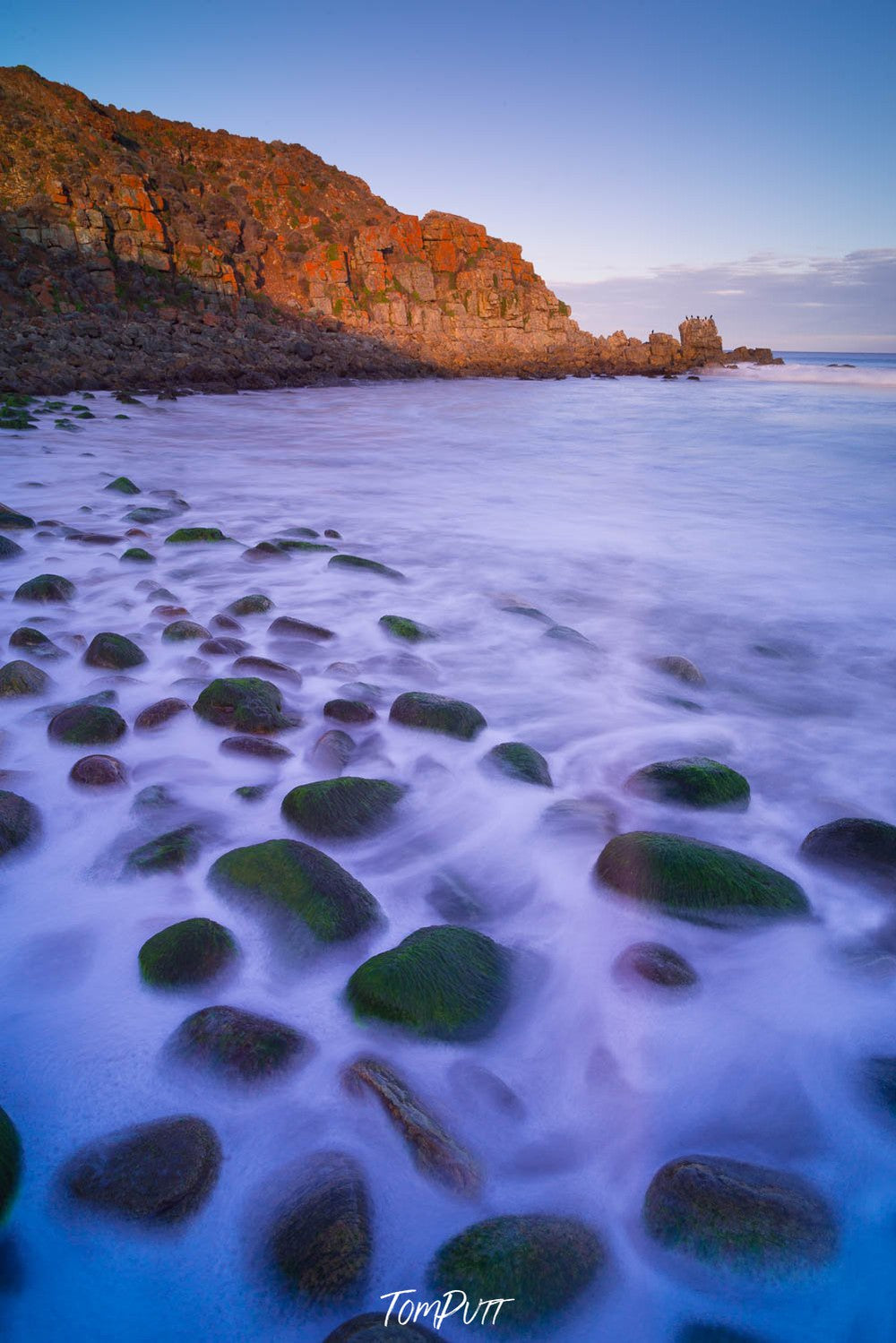 Group of flat circled stones on a beach and a big mountain wall in the background, Lone Pine at Sleaford Bay, Eyre Peninsula SA