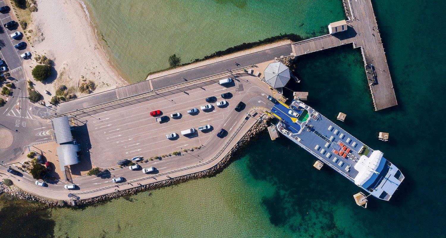Aerial view of a road with some vehicles, built on the edge of a lake, Offloading, Sorrento Ferry - Mornington Peninsula VIC
