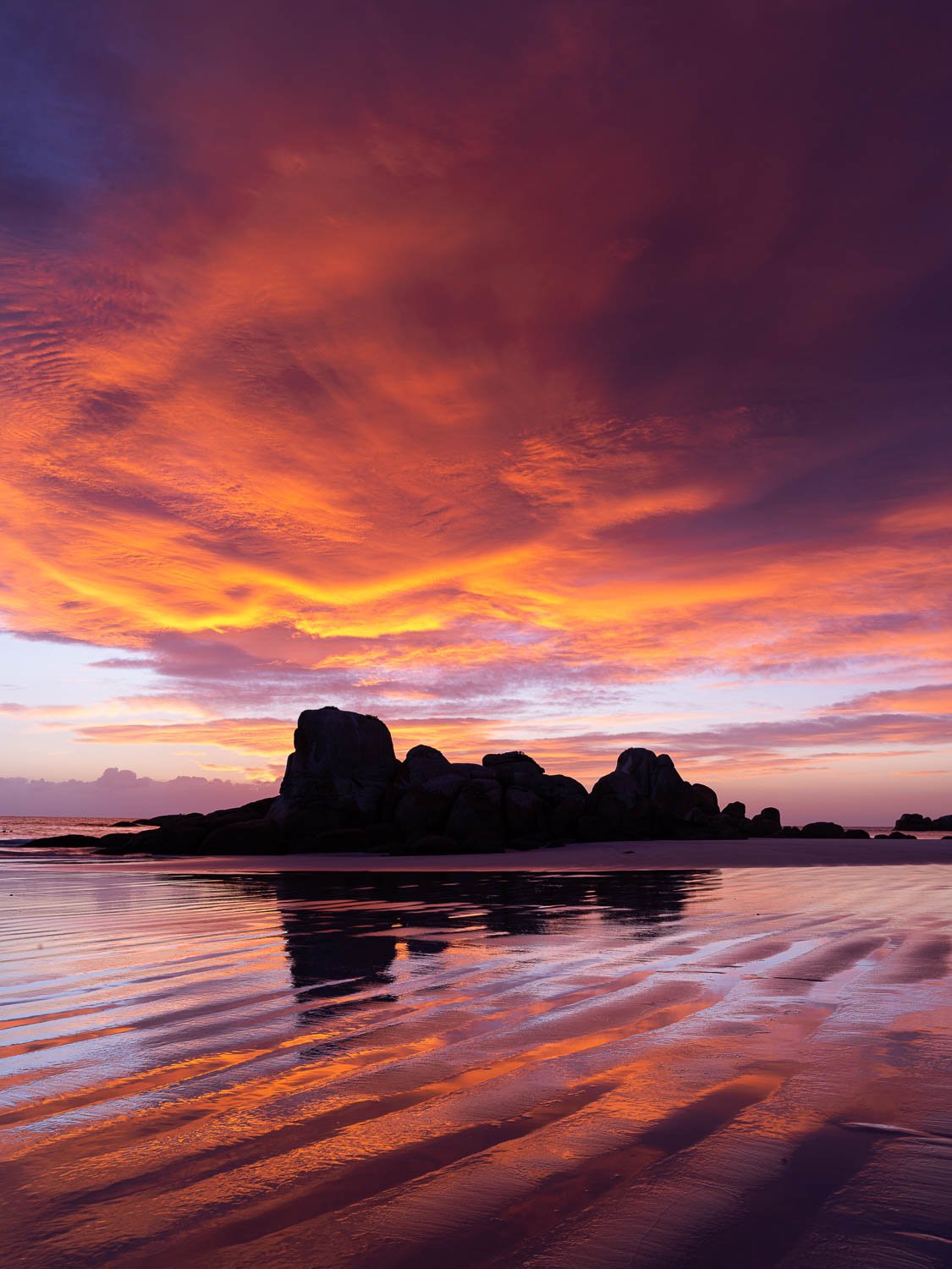 Dark mountains with a dense orangish and reddish effect of clouds over, Picnic Rocks sunrise, Bay of Fires
