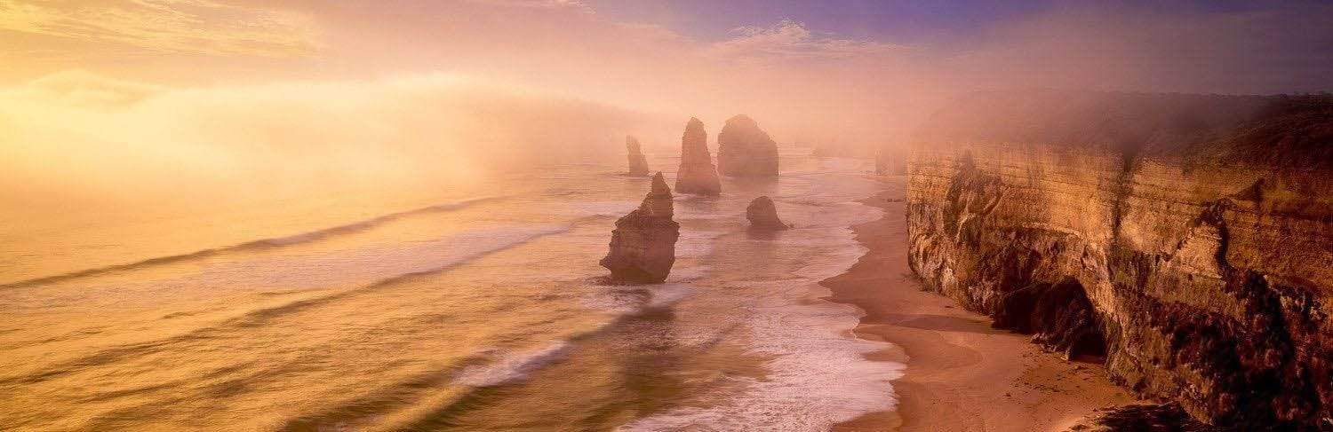 Long shot of a mountain wall and some standing stones below on the beach, Pillars in the Mist, 12 Apostles - Great Ocean Road VIC