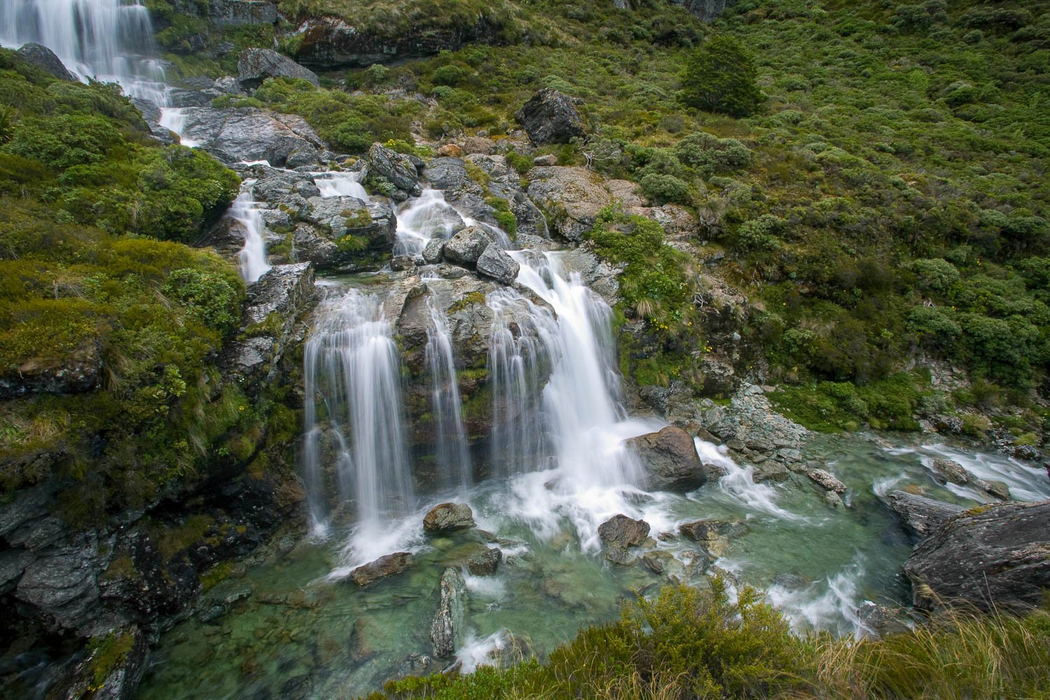 Long shot of nested waterfalls from a green hill point, Routeburn Falls, Routeburn Track - New Zealand