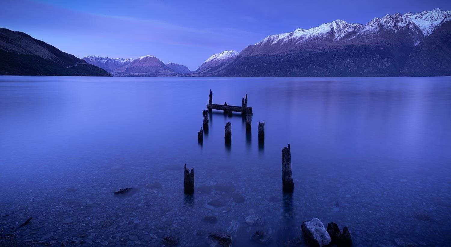 Small wooden sticks in the lake with some mountain walls behind, Ruined Jetty, Glenorchy New Zealand