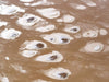 Frying egg-like texture on a beach with some water, Scattered Pebbles