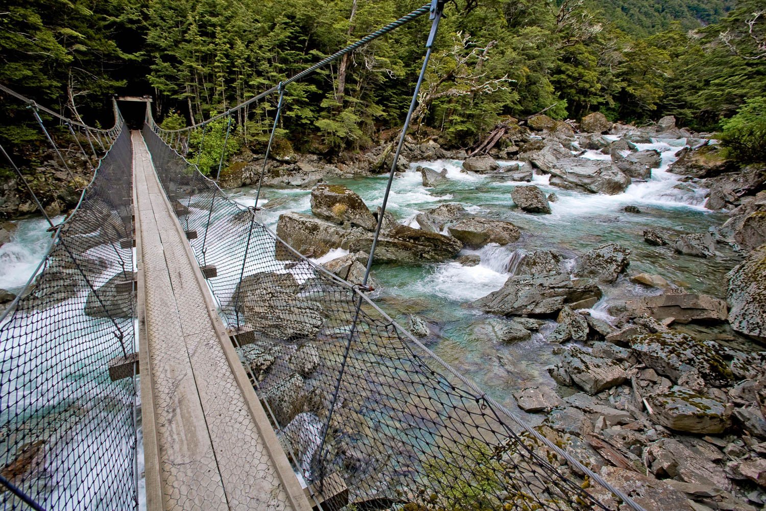 A bridge over a green watercourse with nested steel sidewalls, Swing Bridge over the Route Burn, Routeburn Track - New Zealand
