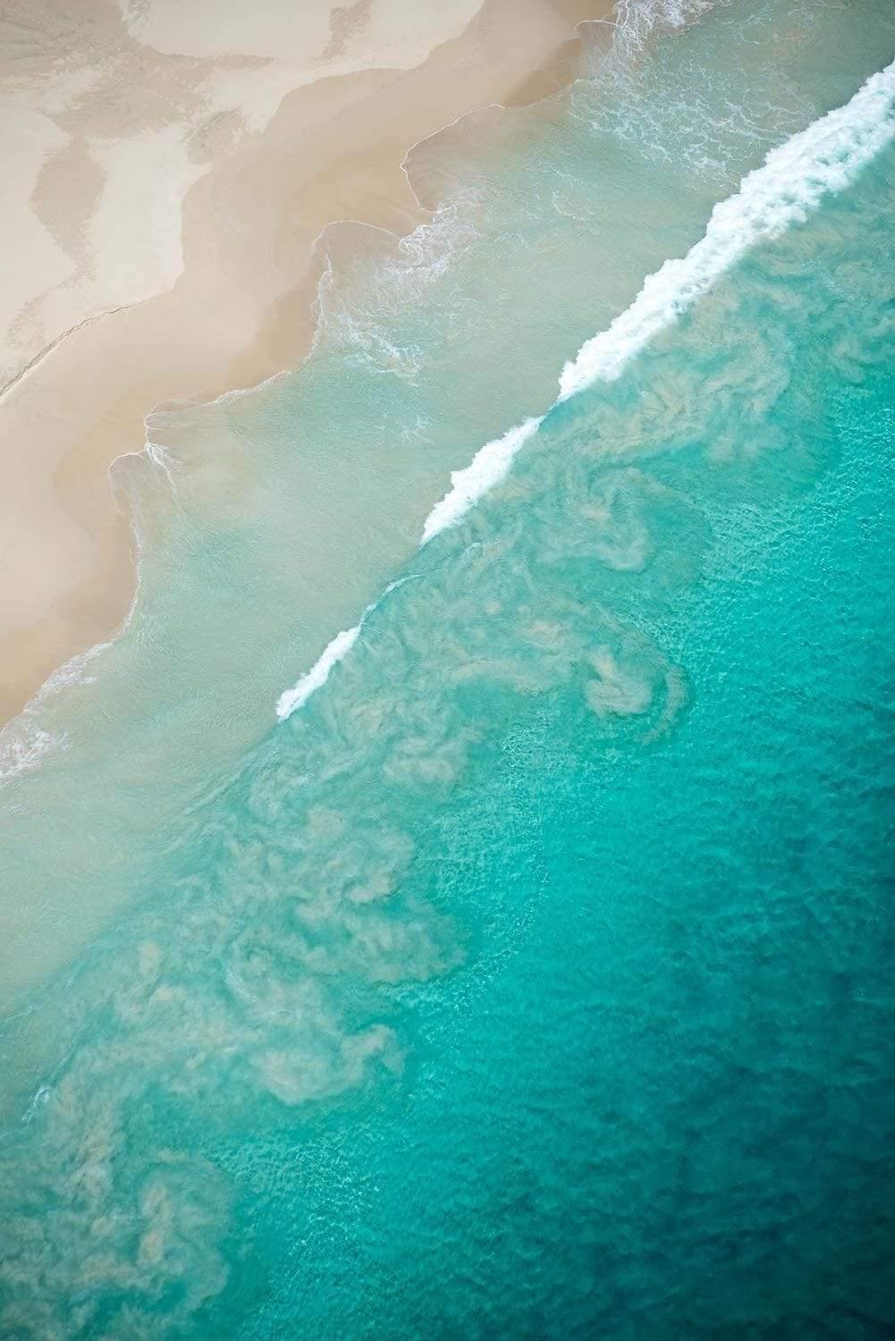 Aerial view of a huge ice-blue sea connecting with a beach-like land, Swirls