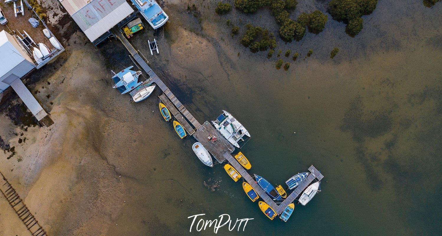 Aerial view of a wooden bridge over the lake, with many boats, rides ready to go, Take Your Pick, Warneet - Mornington Peninsula VIC