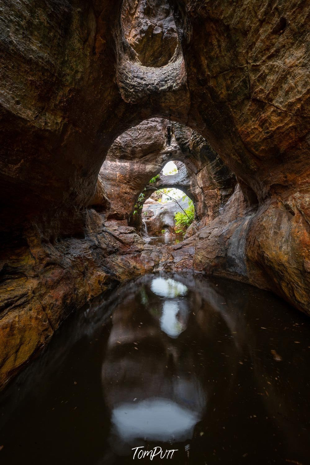 A deep area filled with black mud water surrounded by giant mountain walls forming asymmetric shape in the foreground, Arnhem Land 7 - Northern Territory