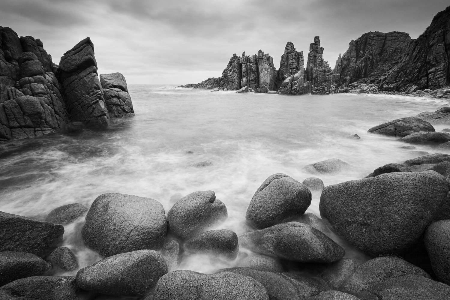A beach with a lot of rounded stones and some standing sculpture of stones behind, The Pinnacles 3, Phillip Island
