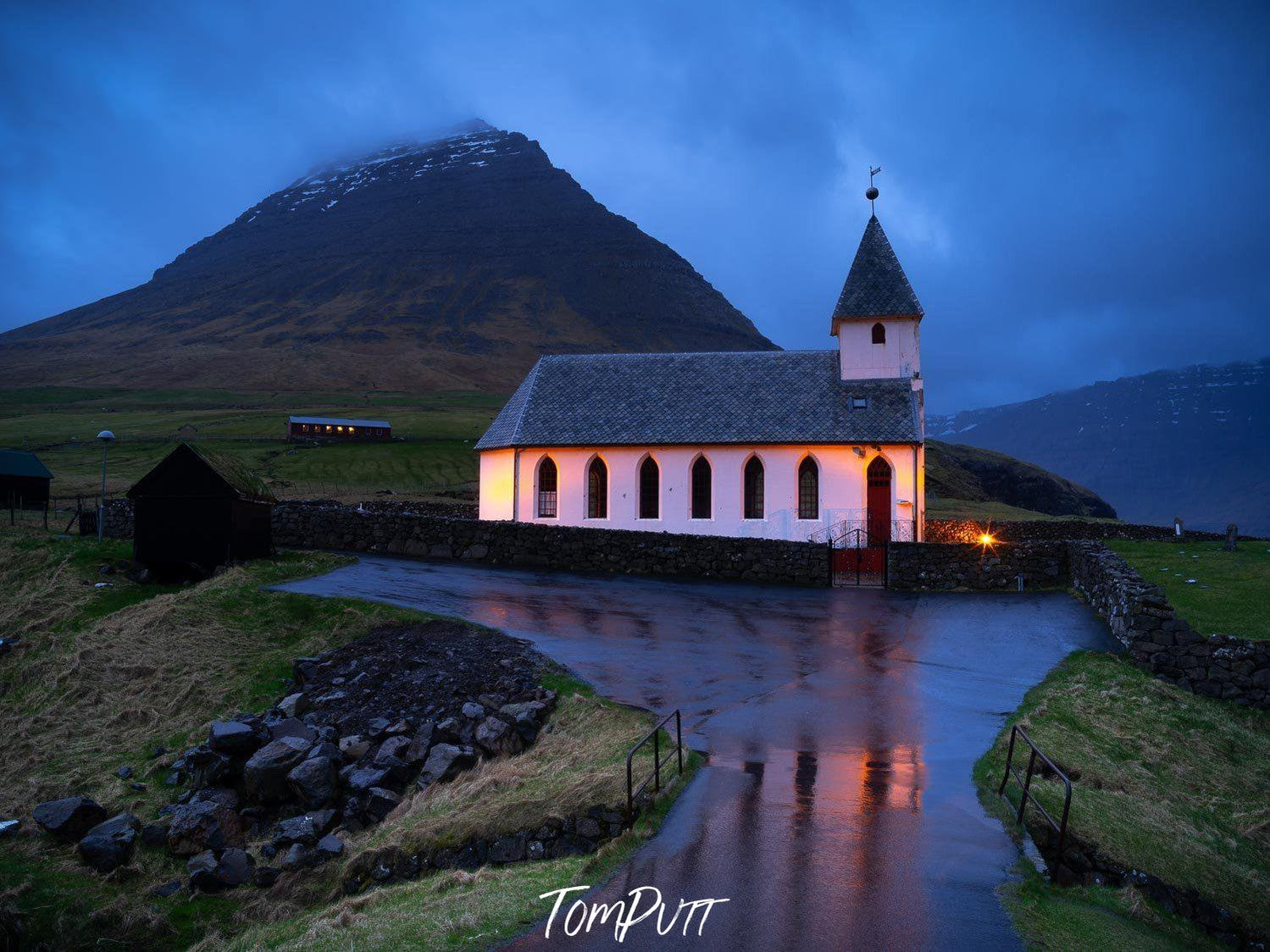 A church built beside a big black mountain with a small lake ahead, Vidareidi Church, Faroe Islands